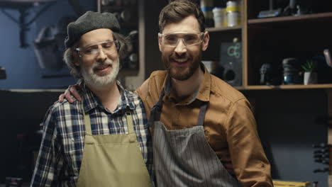 portrait shot of two cheerful father and son in goggles hugging and looking at camera in workshop