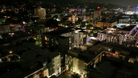 a neighborhood of apartments illuminated by lights in hollywood, los angeles. rising aerial shot.
