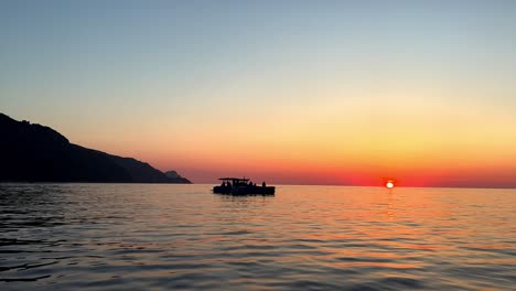 Silhouette-of-navigating-boat-at-sunset-with-sun-on-horizon