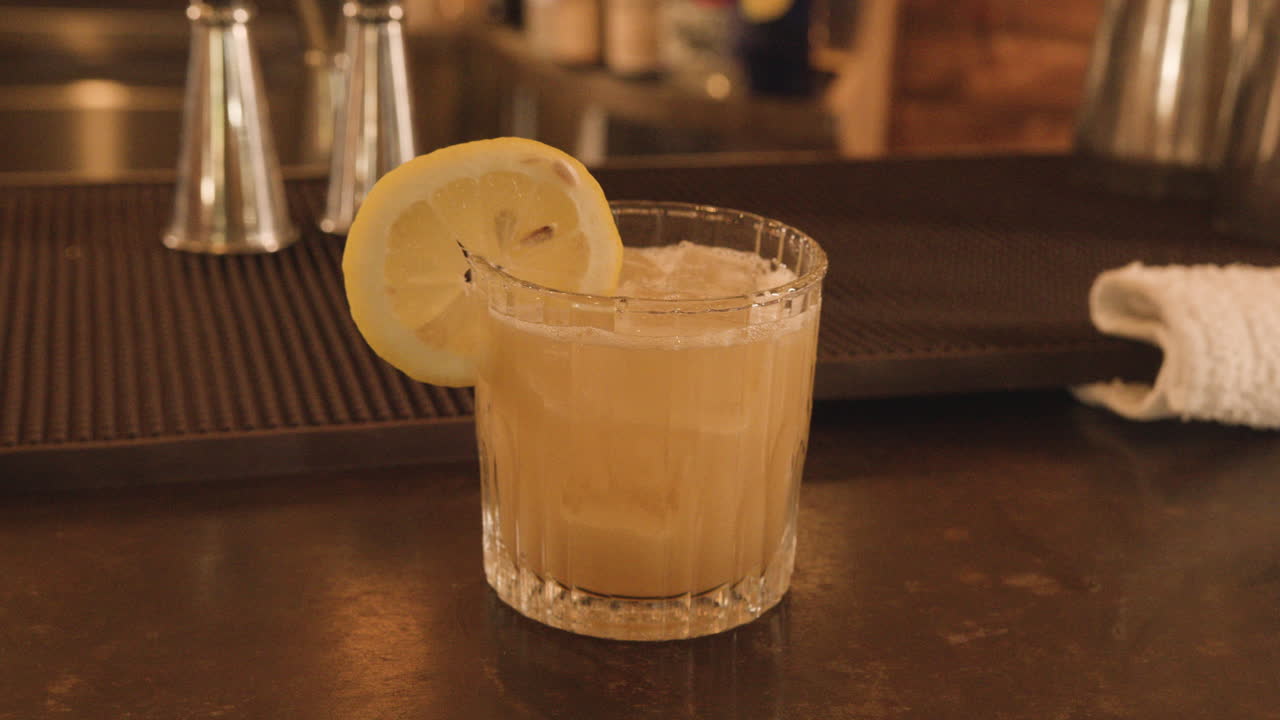 Cocktail glass sitting on bar is picked up toward camera by masculine hand in slow motion