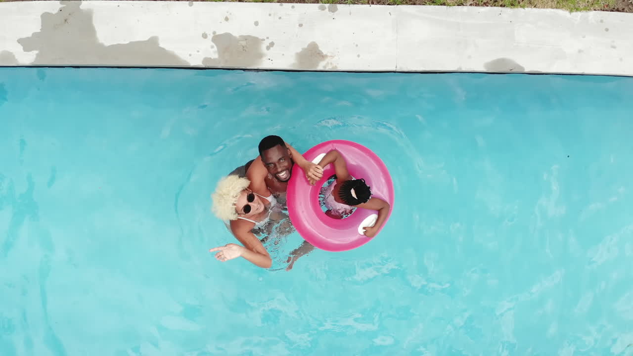 An African American family floats on a pink inflatable ring in a pool at home