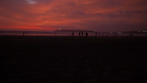 seascape view of people silhouettes on a sandy coastline, during a bright red sunset, on a cloudy evening