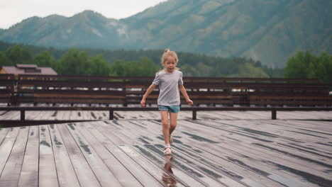 child girl runs along empty wooden deck with small puddles