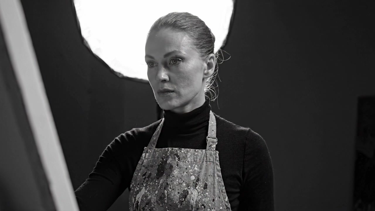 En fokuseret kunstner står foran et lærred, dybt engageret i sin kreative proces under dramatisk belysning, der fremhæver hendes unikke kunstneriske vision og passion.