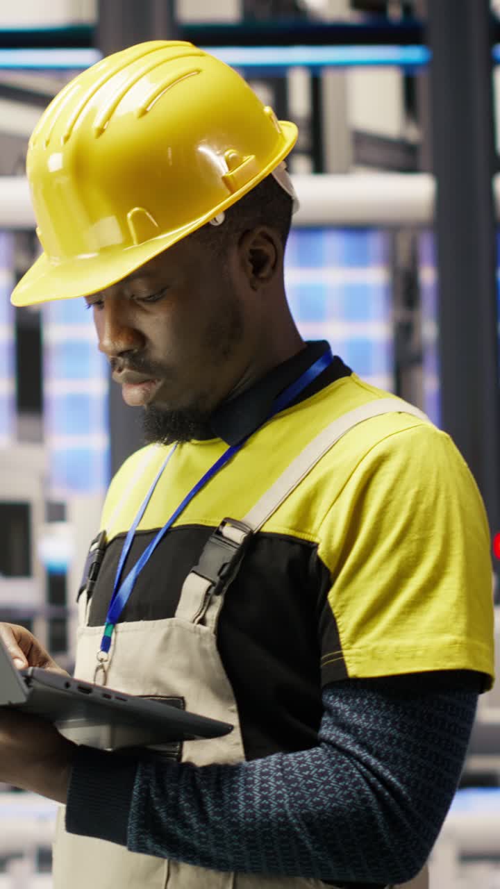 Vertical video Technician in solar panels factory oversees robot assembly lines using laptop