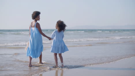 happy woman and daughter talking and hugging each other while walking along beach