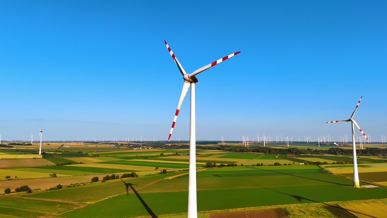 Blades of wind turbines with red stripes rotate in the wind. Aerial view on the fields with wind farms. Green energy concept.