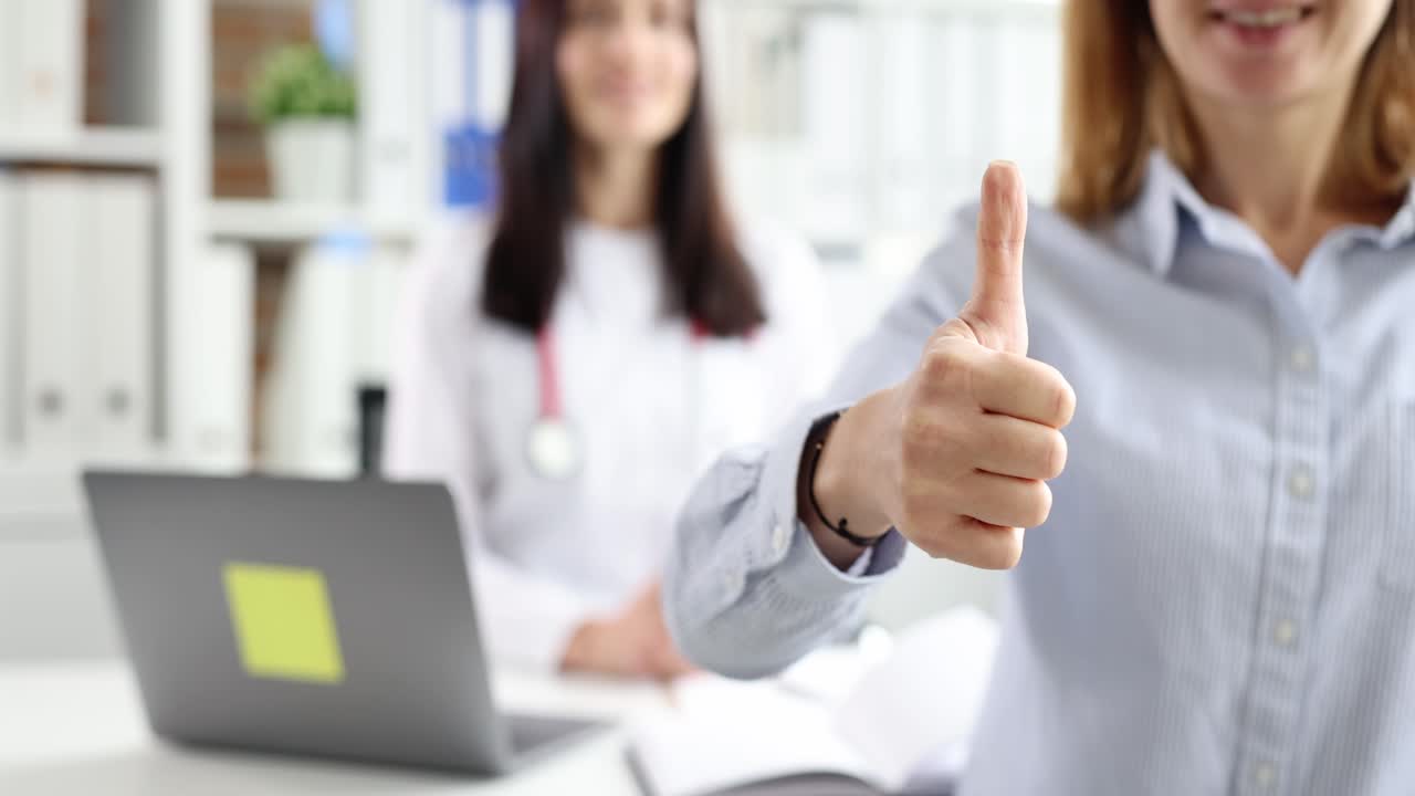 Paciente mujer mostrando el pulgar hacia arriba con un médico de fondo en la clínica, película 4k en cámara lenta