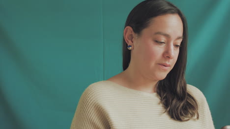 medium shot of a young woman in focus on a professional recording set, with a solid turquoise background.