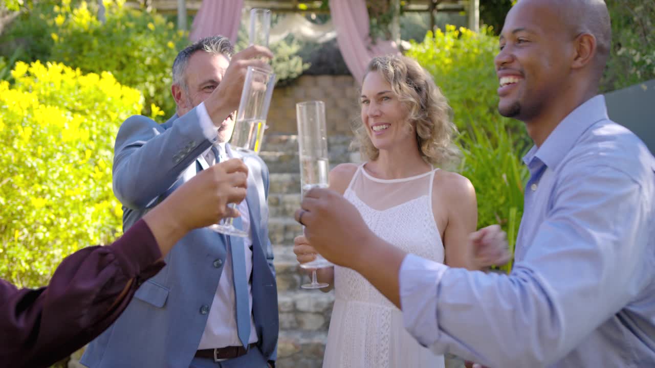 Quattro amici che festeggiano, una coppia che si abbraccia, si bacia sulla guancia e brinda con i calici ai piedi di una scalinata.