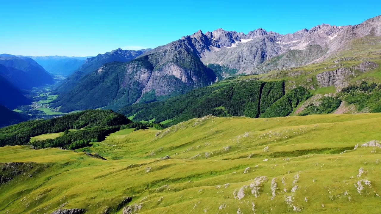 Bred naturskøn udsigt over en frodig grøn alpeeng, der stiger mod barske klippetoppe og skovklædte skråninger under en klar blå himmel i skarpt naturligt dagslys.