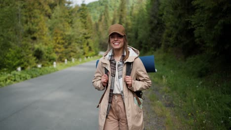 a blonde girl in special clothes for a hiker of light brown color poses near the road being in a mountain forest