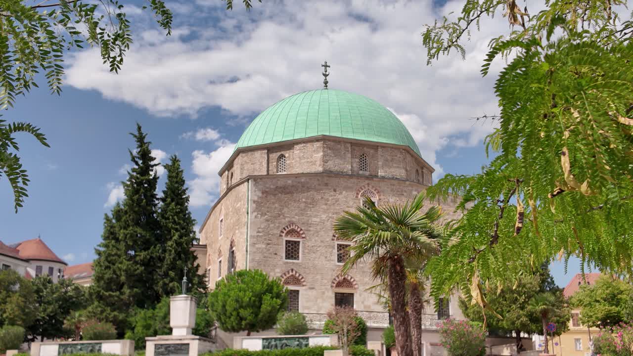 Exterior view of the Mosque of Pasha Qasim in Pécs, beautifully framed by a tree, highlighting its ornate architecture and historic charm