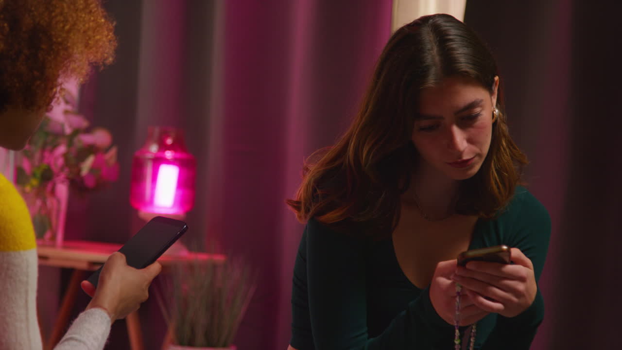보라색 빛이 있는 방에서 스마트폰을 사용하는 두 명의 여성