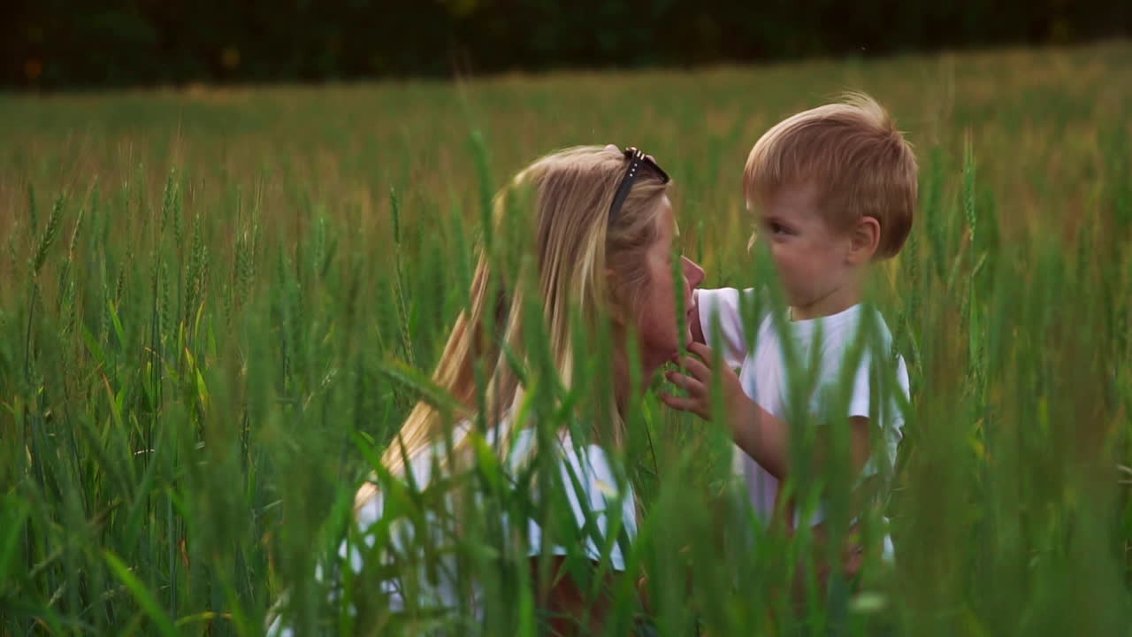 счастливая семья веселится. мальчик с коричневыми кудрявыми волосами и его мать с рыжими волосами показывают палец друг другу. съемка на открытом воздухе