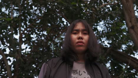 young woman gazing down with curiosity, trees in soft focus background, natural light