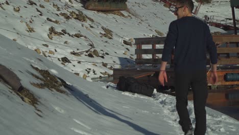 一名男子穿过雪道走向陡峭地形中的木制山屋