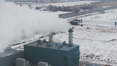 industrial buildings with smokestacks in winter, emitting steam against a snowy landscape, aerial view