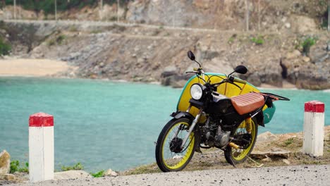 Static-shot-of-parking-motorcycle-carrying-longboard-and-blue-pacific-ocean-bay-in-background