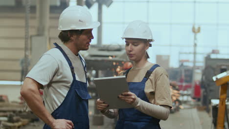 male and female industrial workers using tablet and talking in factory