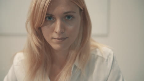 Close-Up-Portrait-Of-Young-Blonde-Woman-Looking-At-Camera-Indoor