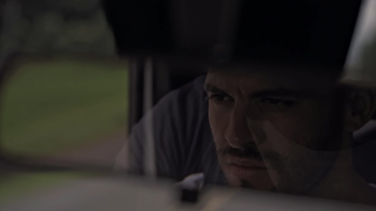 A close-up from the rearview mirror captures a man driving through Costa Rica, with a blurred green landscape outside, filmed during a scenic journey
