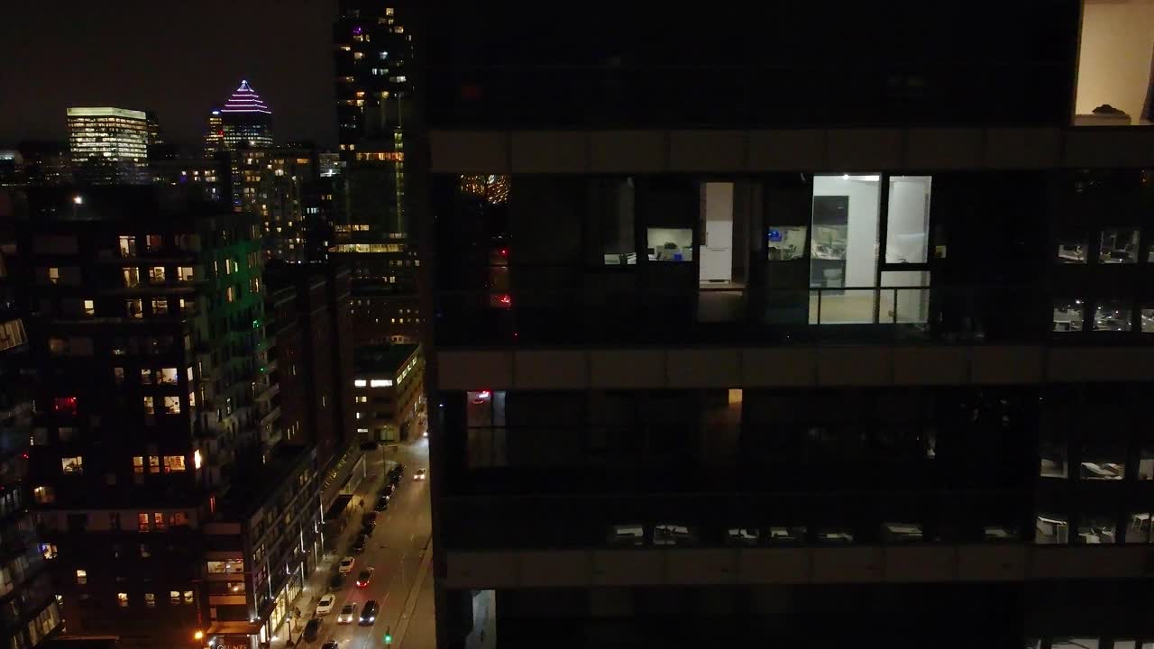 vista nocturna de ventanas de oficinas iluminadas en un rascacielos de montreal, luces de la ciudad en el fondo, trabajo urbano concepto tardío