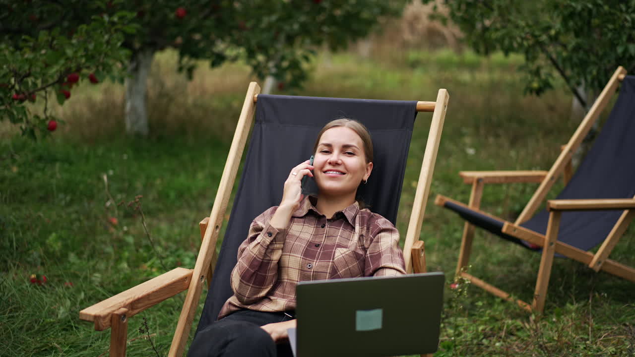 Happy relaxed Caucasian woman calling somebody on the phone. IT specialist working remotely from office in the nature.