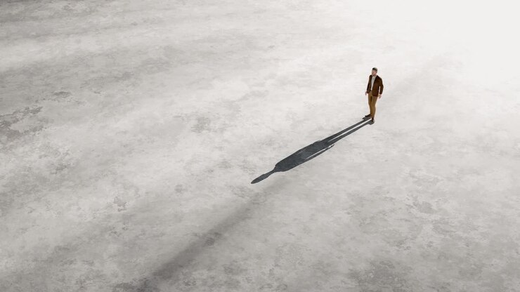 Uomo in piedi da solo su una vasta superficie vuota con un'ombra che si allunga.
