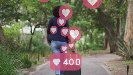 animation of social media heart icons over african american woman riding bicycle in park