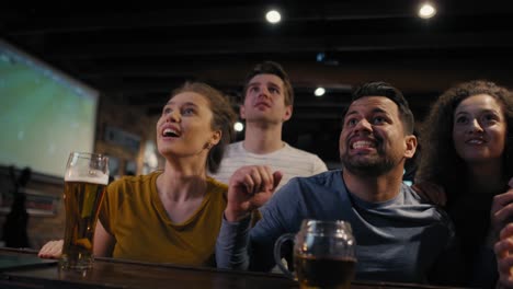 group of friends cheering to soccer match in the pub