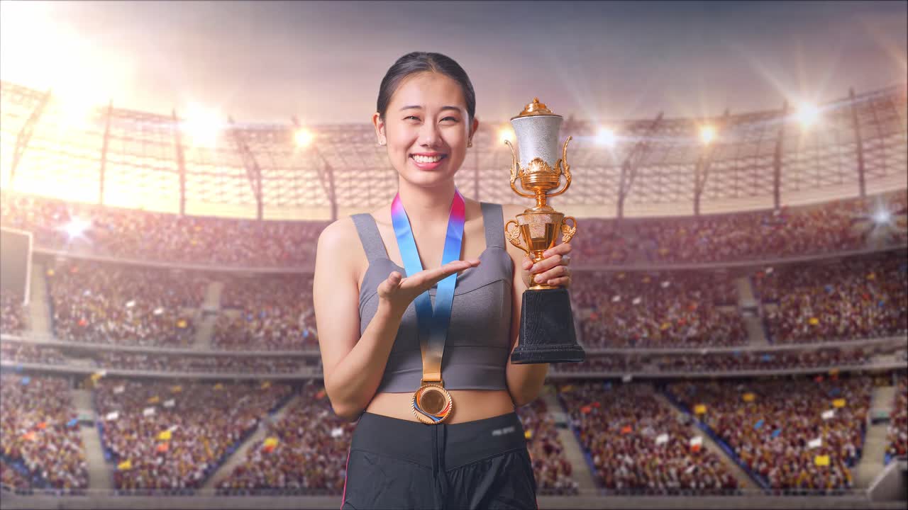Asian Woman With A Gold Medal Pointing To A Gold Trophy In Her Hand And Smiling Being Proud Winning As The First Winner At The Stadium
