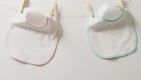 video of close up of two white baby bib with pegs hanging on white background