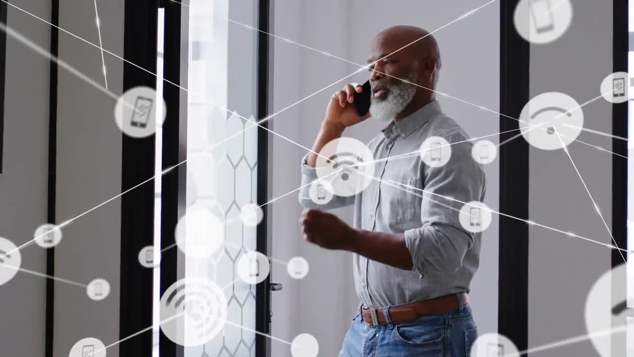 Netværk af digitale ikoner mod afroamerikansk seniorforretningsmand, der taler i smartphone på kontoret