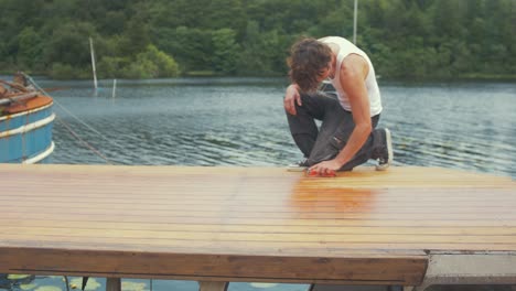 youth walks into frame to start hand sanding roof of wooden boat planking