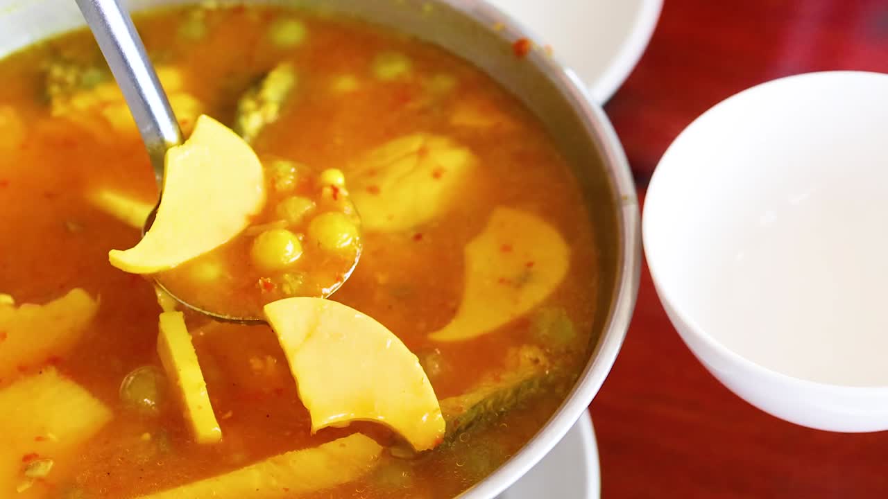 A vibrant orange curry with vegetables is ladled into white bowls, showcasing its rich color and texture.