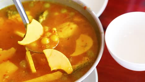 a vibrant orange curry with vegetables is ladled into white bowls, showcasing its rich color and texture.