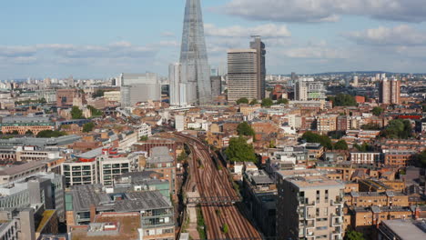 Aerial-view-of-train-driving-on-multitrack-railway-line-through-city.-Tilt-up-reveal-of-The-Shard-skyscraper.-Tall-modern-office-building.-London,-UK