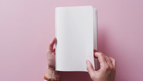 primer plano de la mano hojeando un libro con espacio de copia en un fondo rosa en cámara lenta