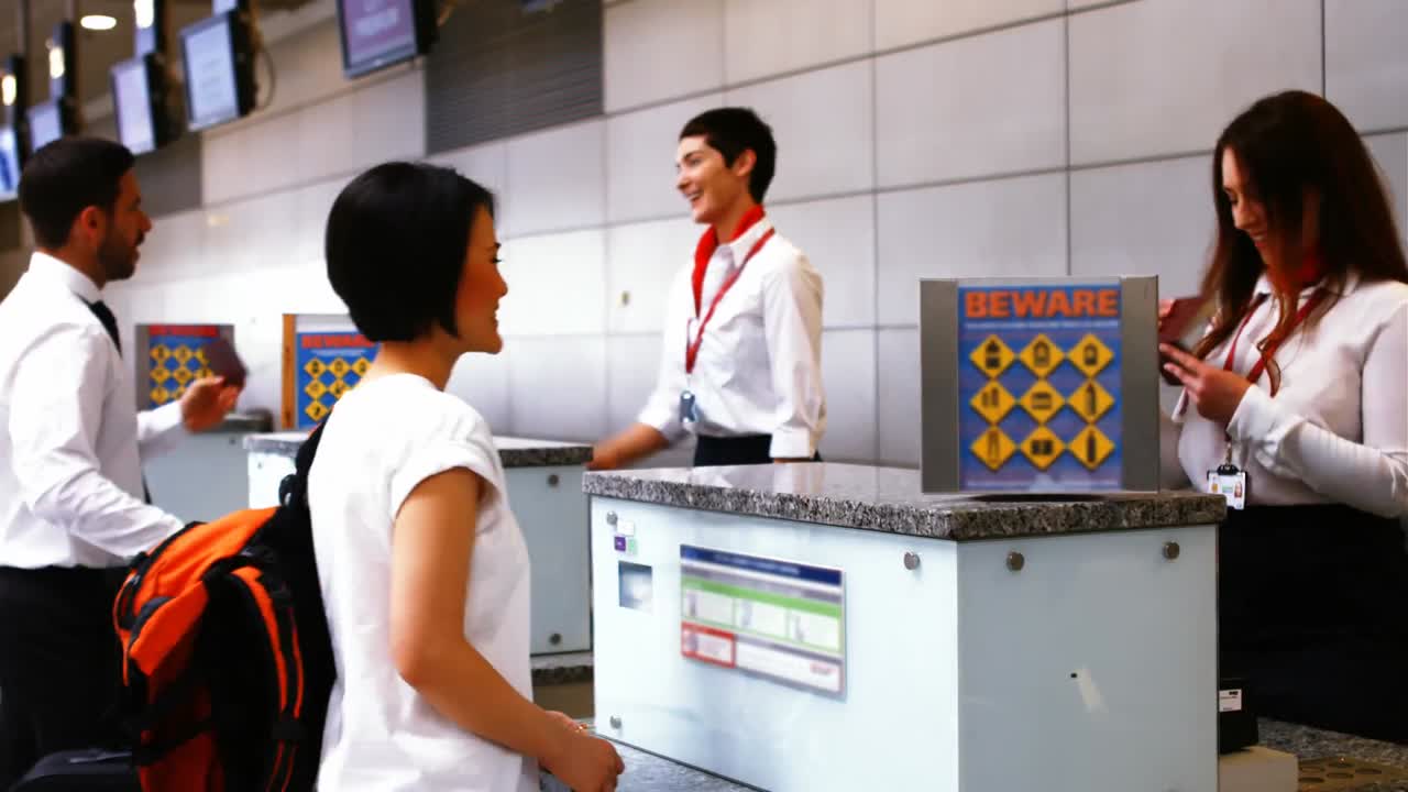 Two female airport staff checking passport and interacting with commuters at check-in desk