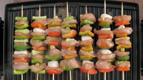 cenital view of seven chicken and vegetables skewers cooking on a hot electric grill