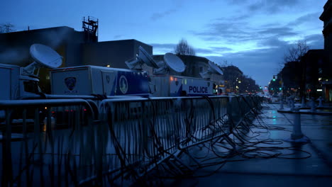 police mobile command center with satellite dishes and barriers on a city street at dusk