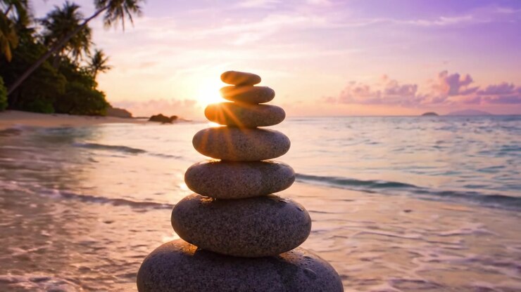 Une vue sereine au coucher du soleil présentant une pile complexe de pierres lisses sur une plage tranquille, entourée de palmiers luxuriants et de douces vagues reflétant une lumière dorée.