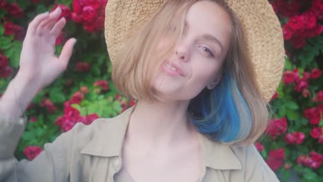 elegant beautiful blonde young woman in a straw hat on the background of a bush of blooming roses