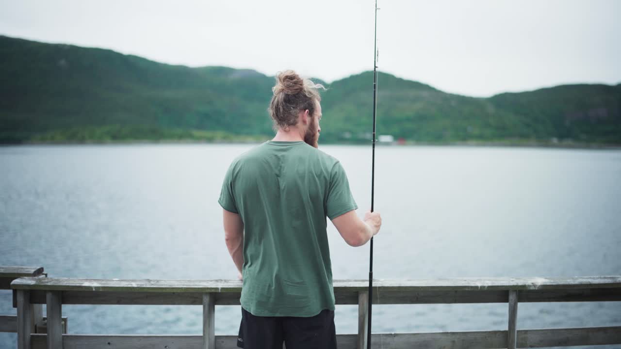 Tampak Belakang Seorang Pria Memegang Joran Pancing di Tepi Danau di Norwegia