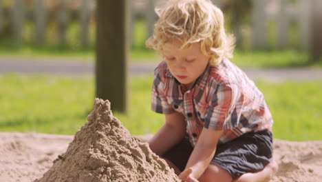 male pupil at montessori school playing in sand pit at breaktime