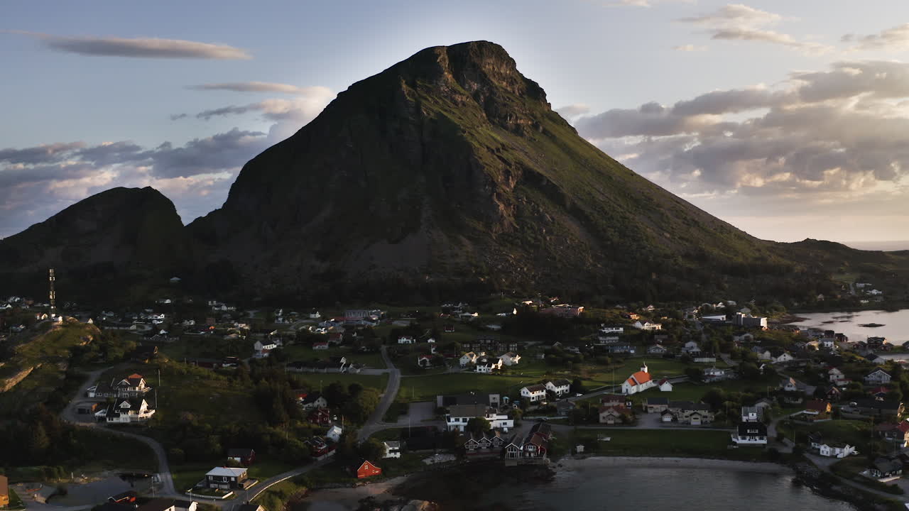 Aerial drone shot panning to the right showing the Island of Lovund with the summit of Lovundfjellet towering over the village. Lovund, Norway