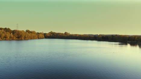 Panorama-of-tranquil-blue-lake-surrounded-by-forest-landscape-in-autumn-colours