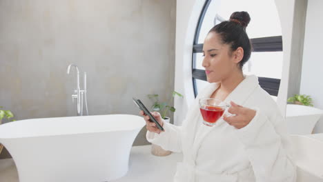 relaxing in spa, asian woman in bathrobe holding smartphone and drinking tea, at home, copy space