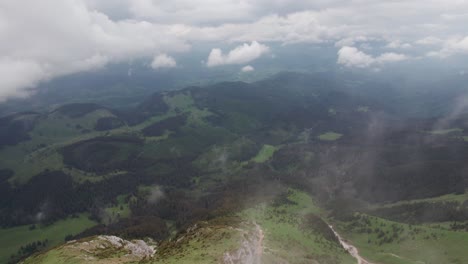 A-mountain-range-with-clouds-hovering-over-lush-forests-at-high-altitude,-tranquil-scenery,-aerial-view